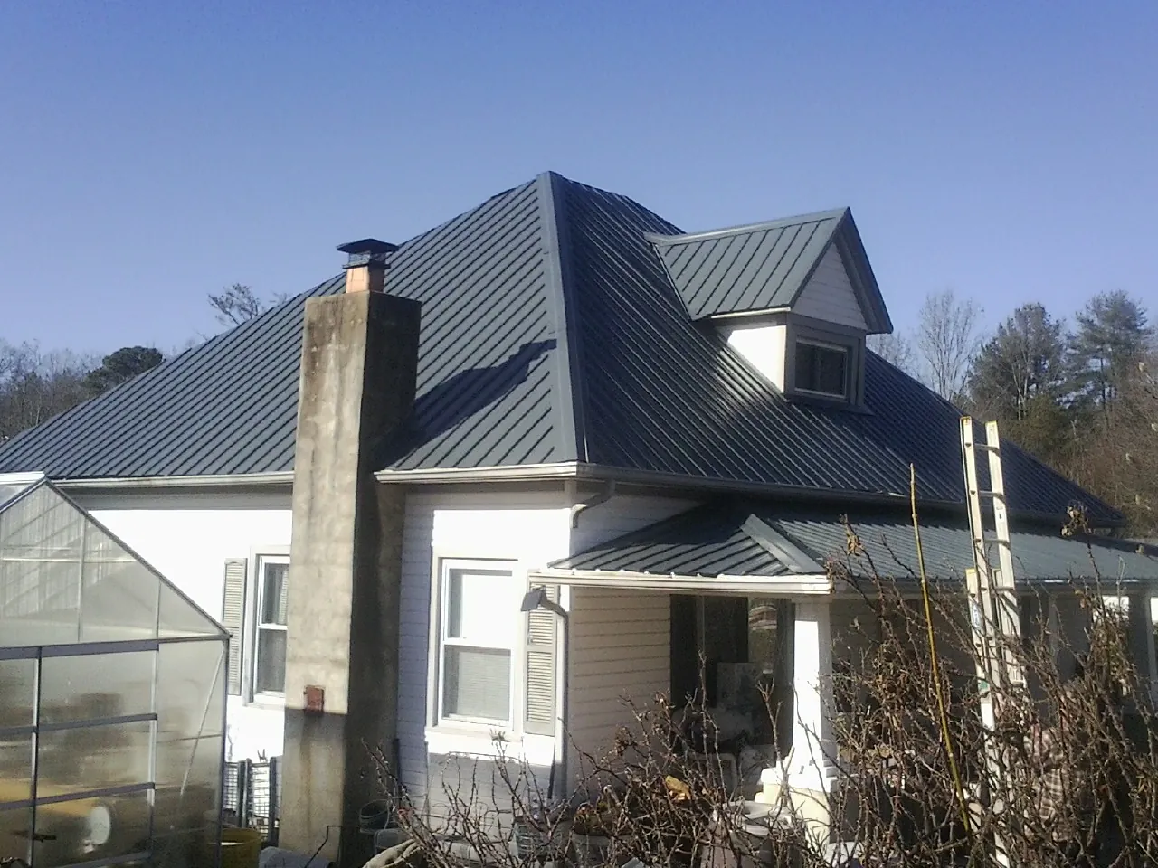 Dark blue standing seam metal roof on a white farmhouse with dormer — Slate & Tile Roof Repair by Roofing Brothers in Groveland