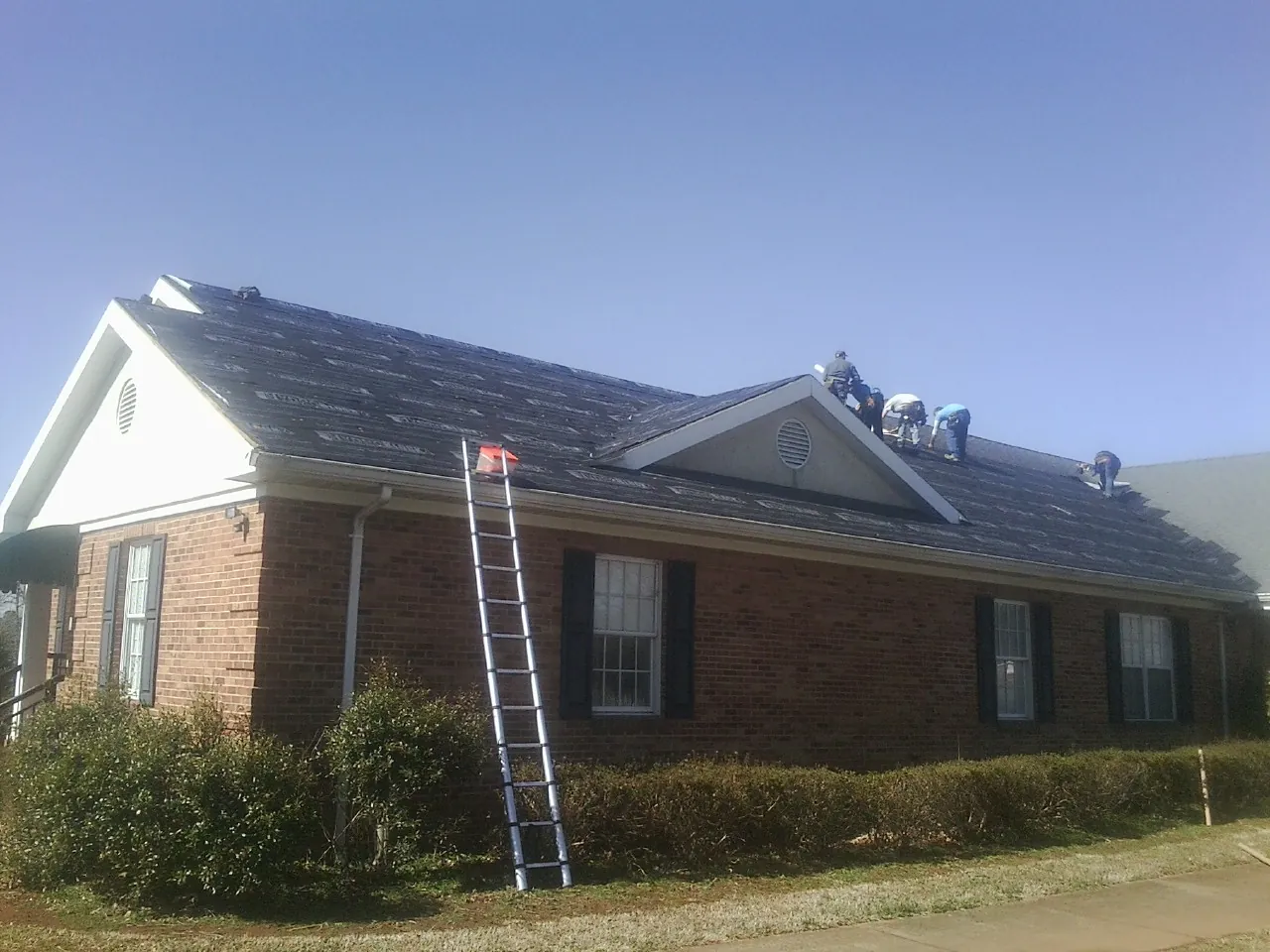 Crew tearing shingles off a brick ranch roof with a ladder set — Metal Roof Repair work by our crew in Groveland